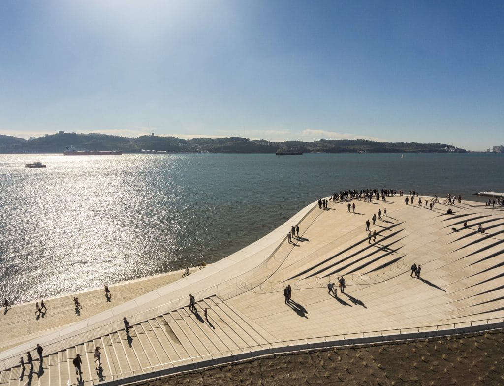 Plataforma branca do MAAT estendendo-se sobre o rio Tejo com pessoas caminhando e apreciando a vista para a água brilhando ao sol, passeio moderno e fotogénico para adolescentes em Lisboa | 10 melhores passeios para adolescentes em Lisboa #4